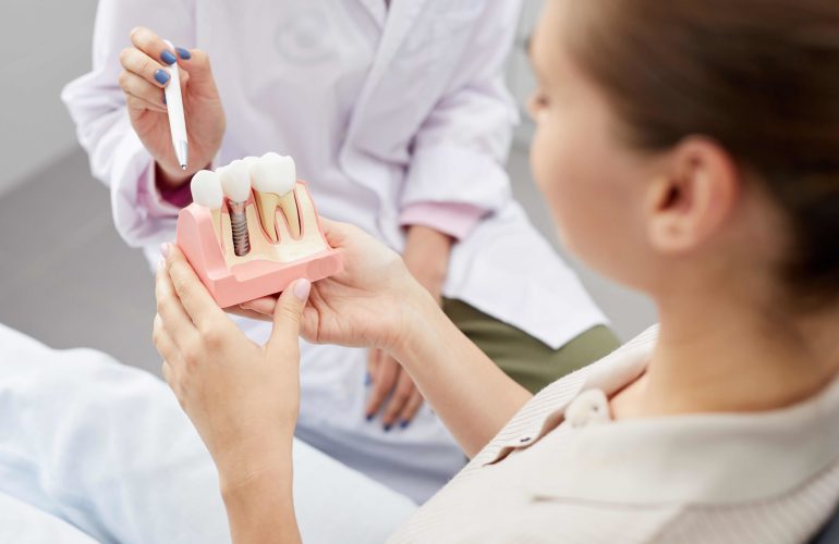 Closeup of unrecognizable female doctor pointing at tooth model while consulting patient, copy space